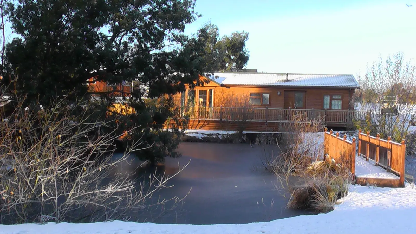 A wooden house with a balcony and snow-covered surroundings, trees, and a clear sky in a winter landscape.