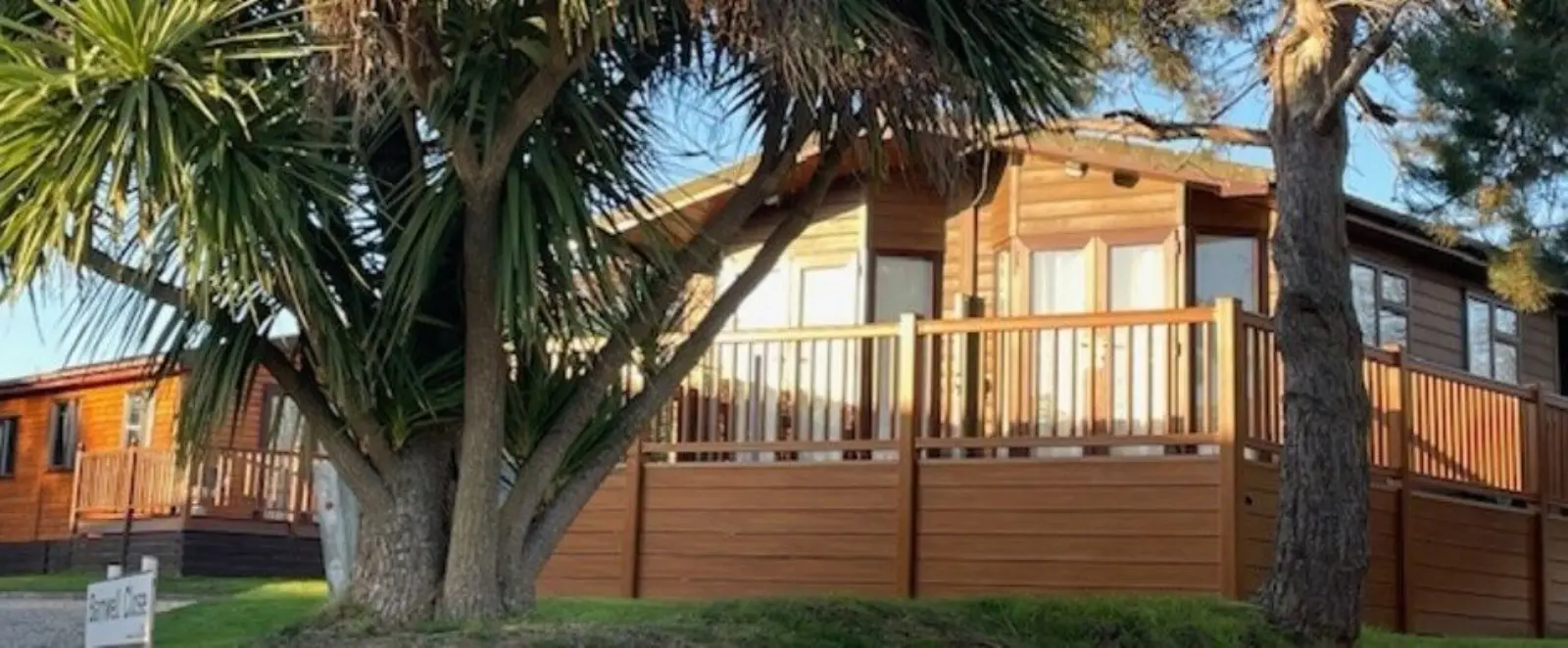 A wooden house with a spacious balcony, surrounded by trees and greenery, under a clear sky during daytime.