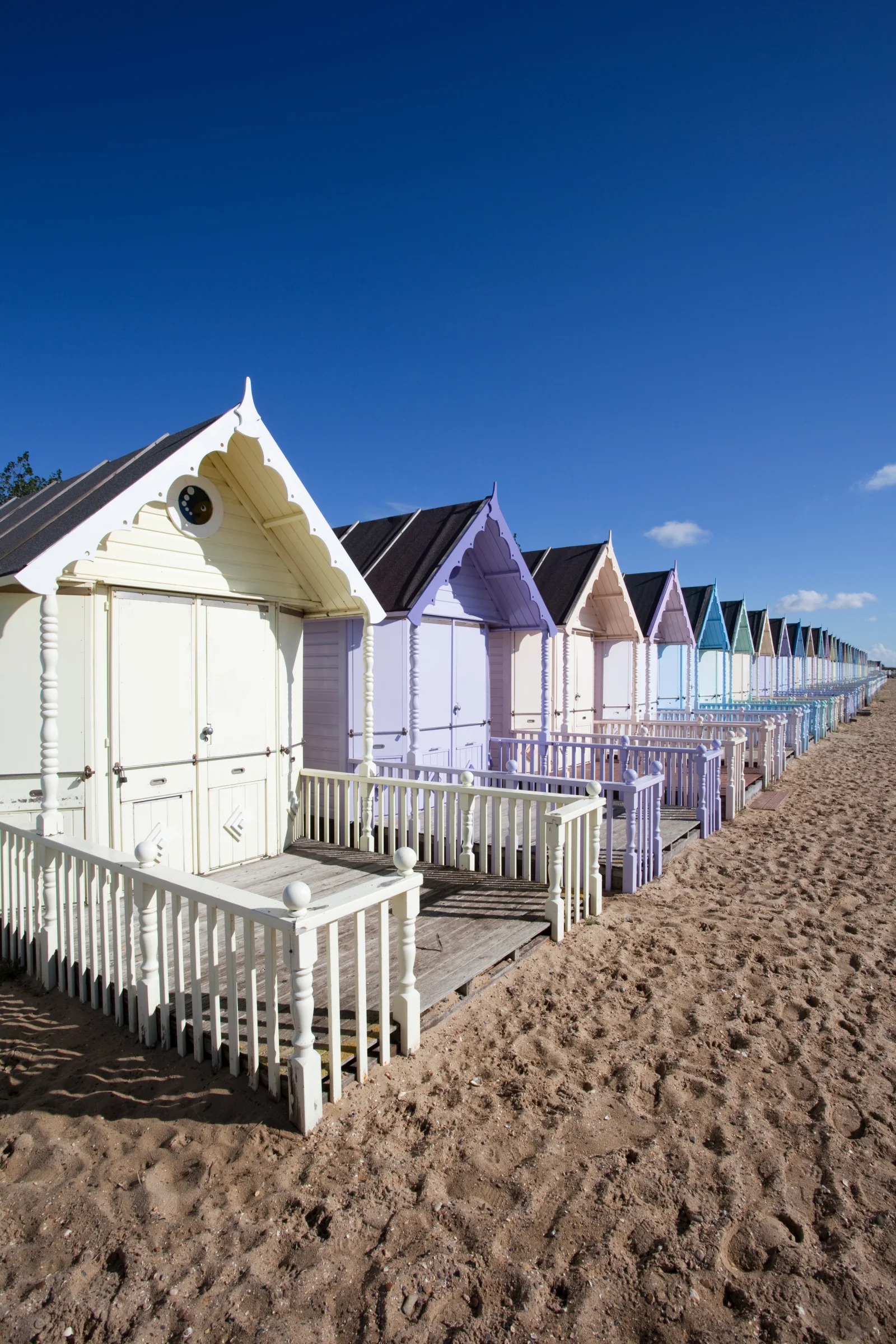 Colorful beach huts with white fences on a sandy shore under a bright blue sky.
