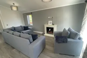 Living room with two light gray sofas, a black fireplace, a small window, and a ceiling light fixture. The room has gray walls and wood flooring.