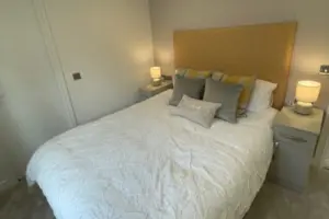 A neatly made bed with a fabric headboard, multiple pillows, and two bedside tables with lamps in a cozy, softly lit bedroom.