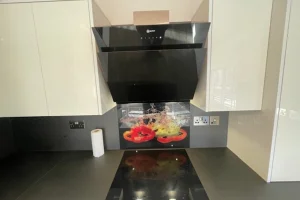 A modern kitchen with black countertops, a black range hood, white cabinets, and a backsplash depicting colorful peppers and vegetables.