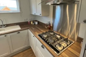 Kitchen with white cabinets, wooden countertop, gas stove, stainless steel backsplash, and a window above the sink.