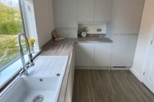 A modern kitchen with white cabinets, a wood countertop, a sink by the window, and a small scale on the countertop.