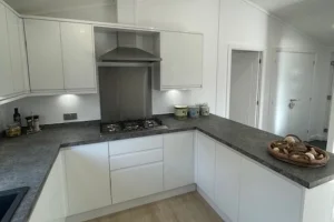 White kitchen with gray countertops, built-in cabinets, a stove with a vent, and a basket of mushrooms on the counter.