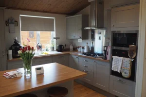 A cozy kitchen with gray cabinets, a wooden island with stools, a window above the sink, and various appliances including a microwave, oven, and gas stove.