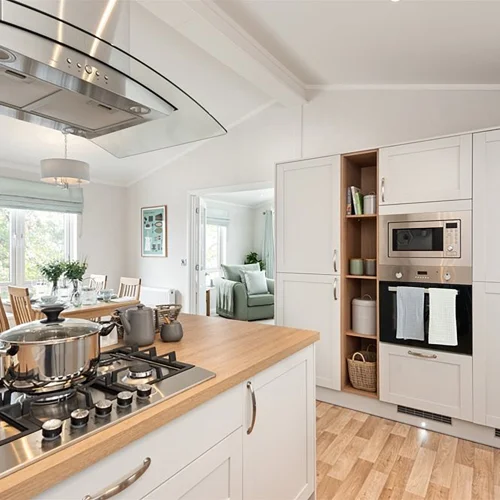 Kitchen with white cabinets, a wooden countertop, stainless steel appliances, and a view into a dining area with a table and green sofa beyond.