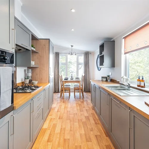 Bright kitchen with grey cabinets, wooden countertops, and a dining area at the back, featuring large windows and natural light.