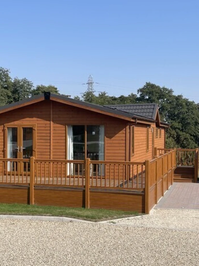 A wooden house with a spacious deck, outdoor storage shed, set in a green landscape with trees and a clear blue sky.