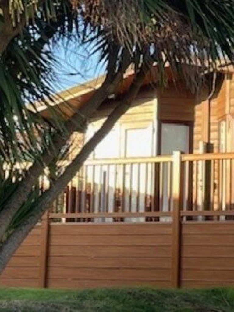 A wooden house with a spacious balcony, surrounded by trees and greenery, under a clear sky during daytime.